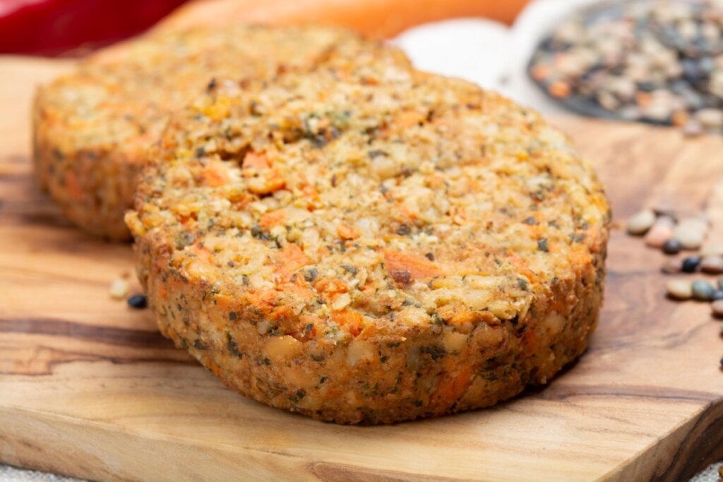 Hambúrguer de lentilha com cenoura e linhaça servido em tábua de madeira em cima de mesa de madeira