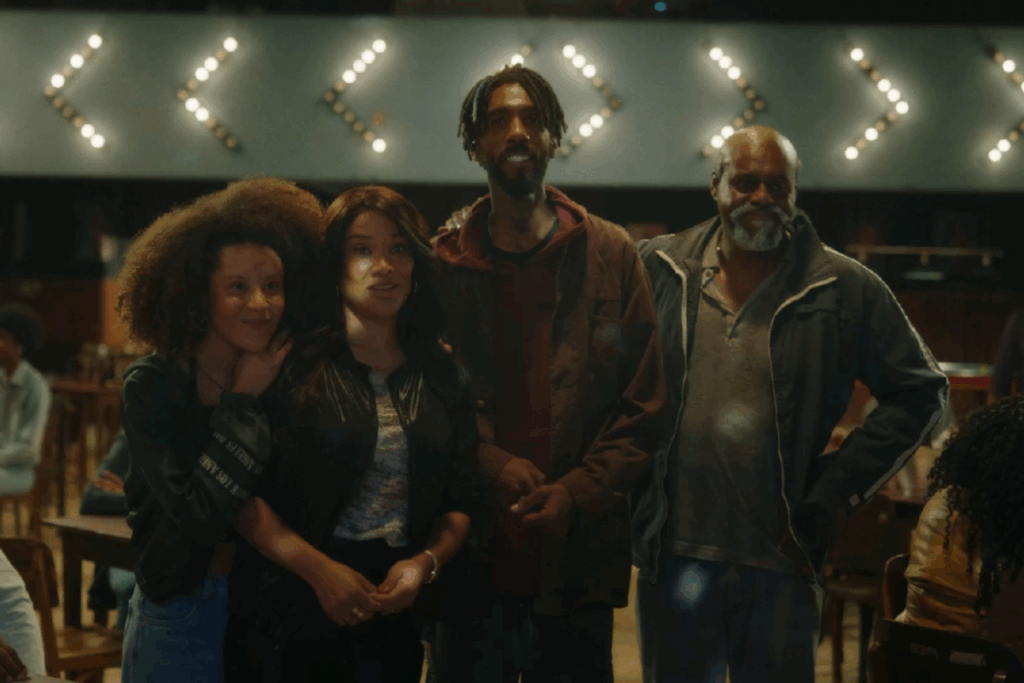 Duas mulheres jovens, um homem adulto e um homem mais velho lado a lado em um salão iluminado