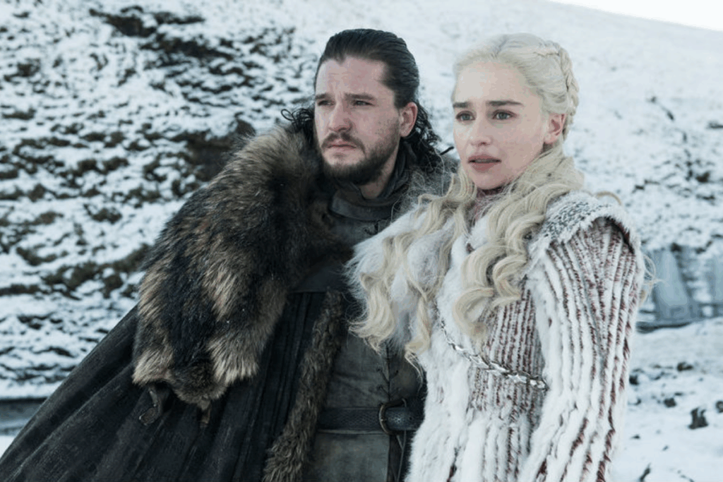 A imagem retrata dois personagens da série Game of Thrones; Eles aparecem lado a lado em um cenário coberto de neve, vestindo trajes típicos do Norte, feitos de peles e tecidos pesados, o que reforça o contexto de guerra, sobrevivência e liderança