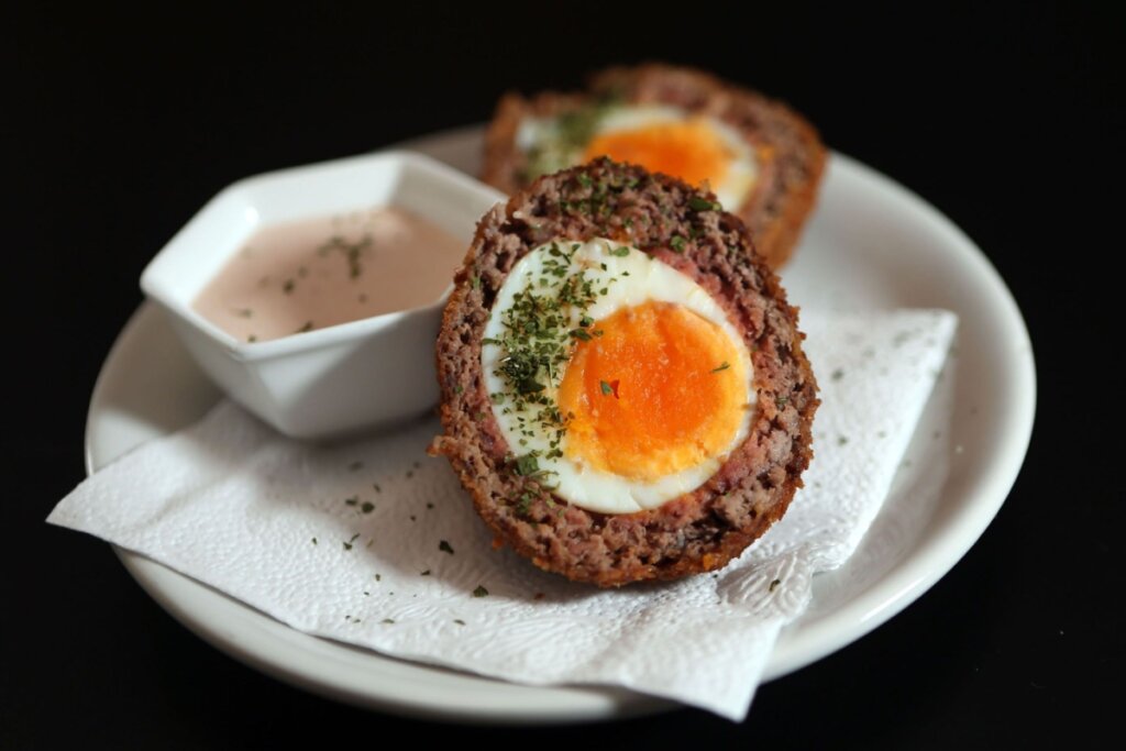 Bolovo cortado ao meio em prato de porcelana branco e ao lado de recipiente com molho rosé 