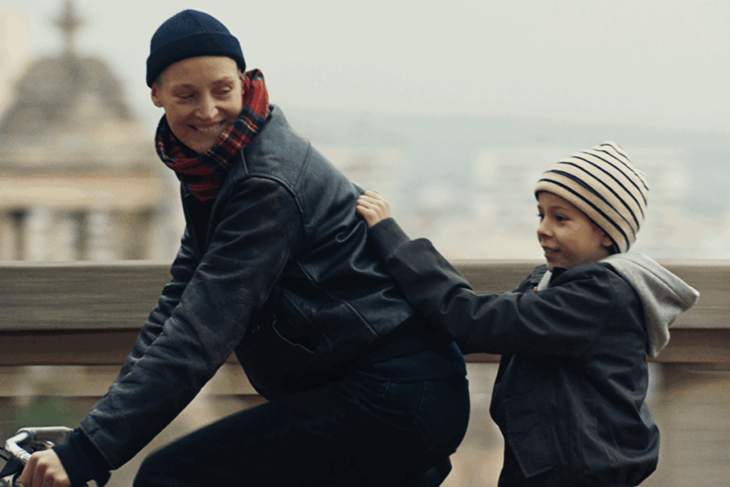 Mulher andando de bicicleta enquanto uma criança, sentada atrás, segura em suas costas
