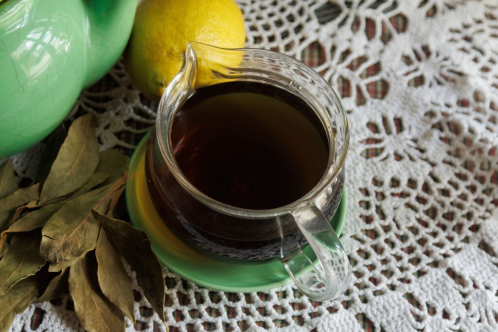 Para que serve o chá de louro? 3 receitas para incluir no dia a dia 5 Xícara de chá com chá de louro ao lado de folhas de louro secas e limão-siciliano