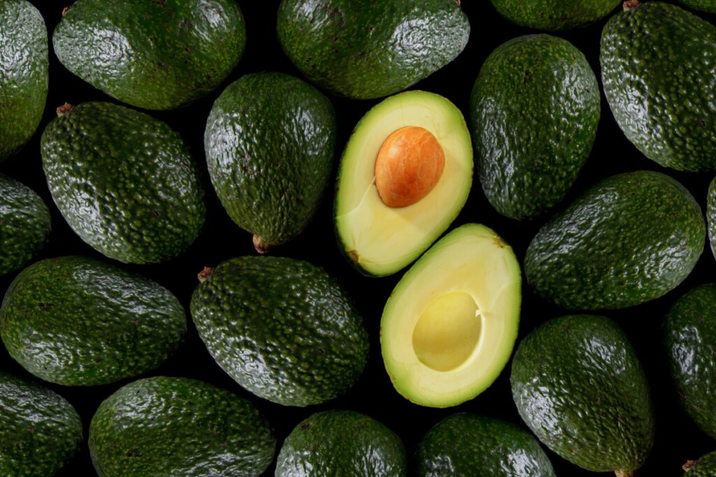 10 alimentos que não podem faltar na dieta da mulher 50 Diversos abacates juntos com casca verde. abacate partido ao meio em cima deles