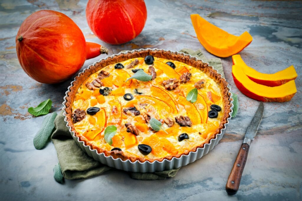 7 receitas práticas de quiches para a Páscoa 5 Quiche de abóbora com nozes e azeitonas em cima de uma mesa cinza com pedaços de abóbora