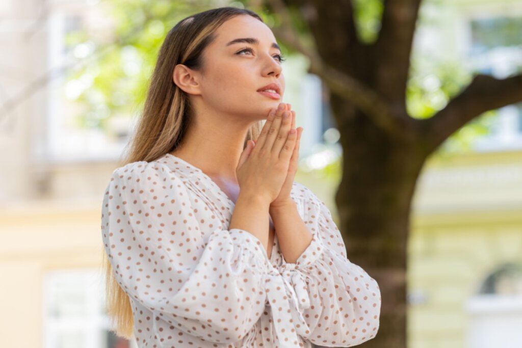 mulher loira com cabelo longo, mãos juntas e olhando para cima