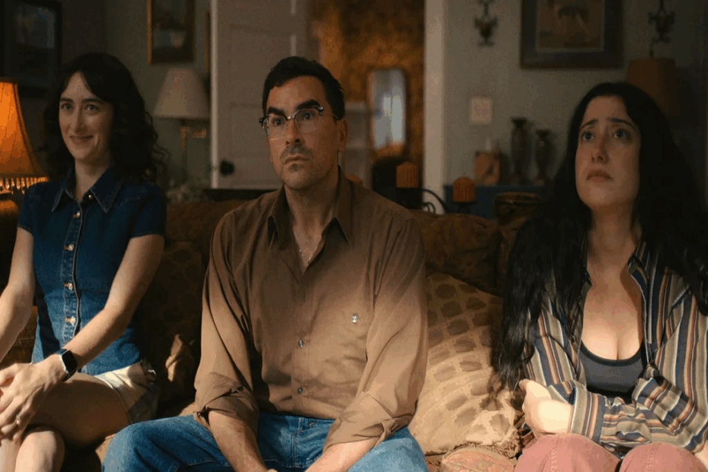 Netflix: lançamentos da semana entre 06 e 12 de abril de 2026 27 Duas mulheres e um homem sentados no sofá, uma das mulheres tem o cabelo solto, está usando uma regata jeans e short branco e está sorrindo, o homem está usando uma camisa de manga longa bege, calça jeans e óculos preto e tem o cabelo curto, e a outra mulher está usando uma calça rosa, blusa listrada e regata preta e está com o cabelo solto